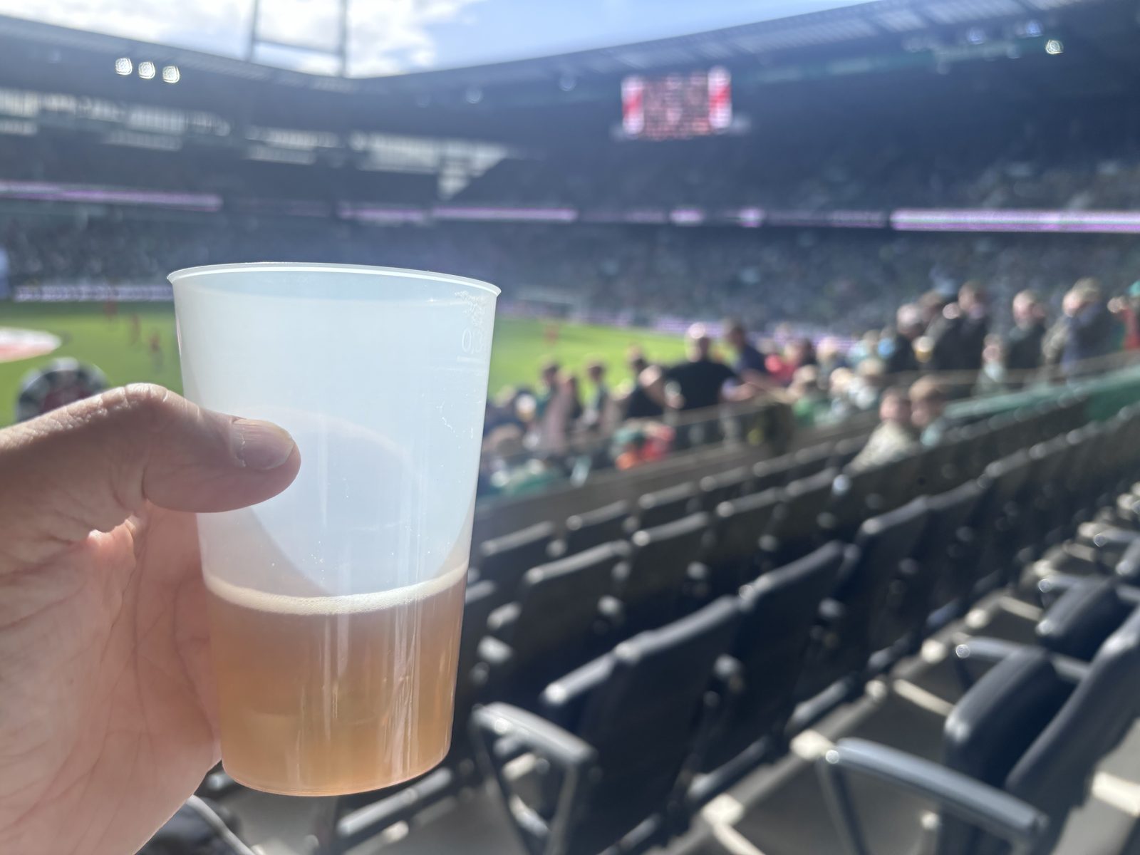 Bierbecher in der Hand vor den Rängen und dem Rasen des Weserstadions.