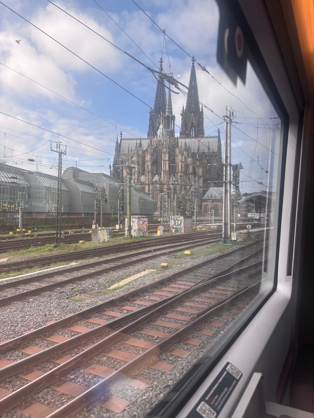 Blick aus einem Zugfenster über Gleise und Oberleitungen auf den Kölner Dom.
