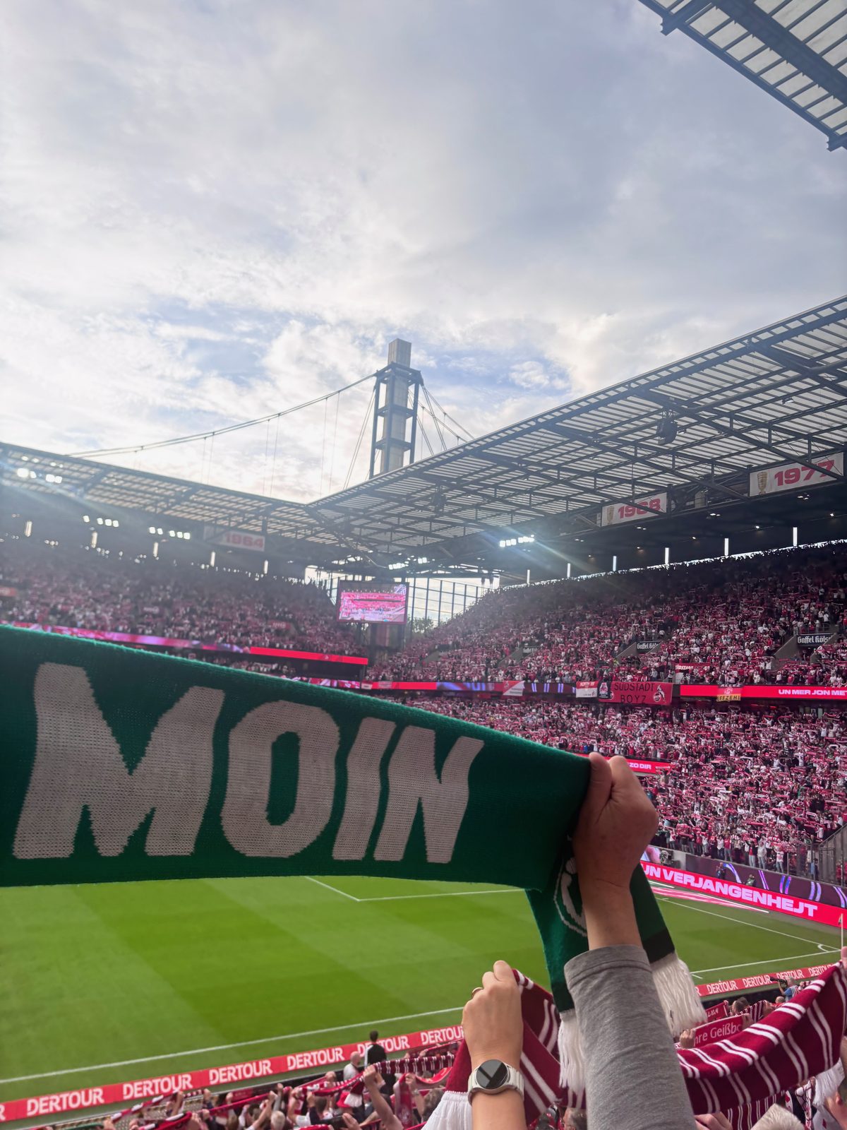 Ein grün-weißer Schal mit dem Wort MOIN wird über der Tribüne des RheinEnergieStadions hochgehalten, dahinter die rot-weißen Ränge.