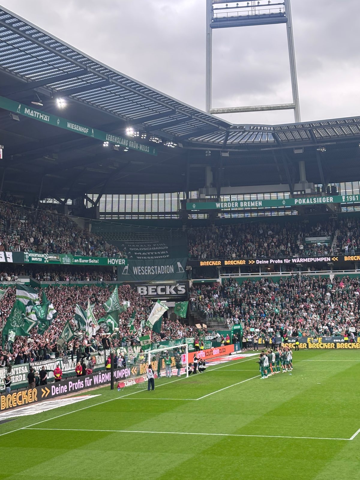 Die Werder-Mannschaft steht nach dem Abpfiff in einer Reihe auf dem Rasen vor der Ostkurve des Weserstadions, in der Kurve werden grün-weiße Fahnen geschwenkt.