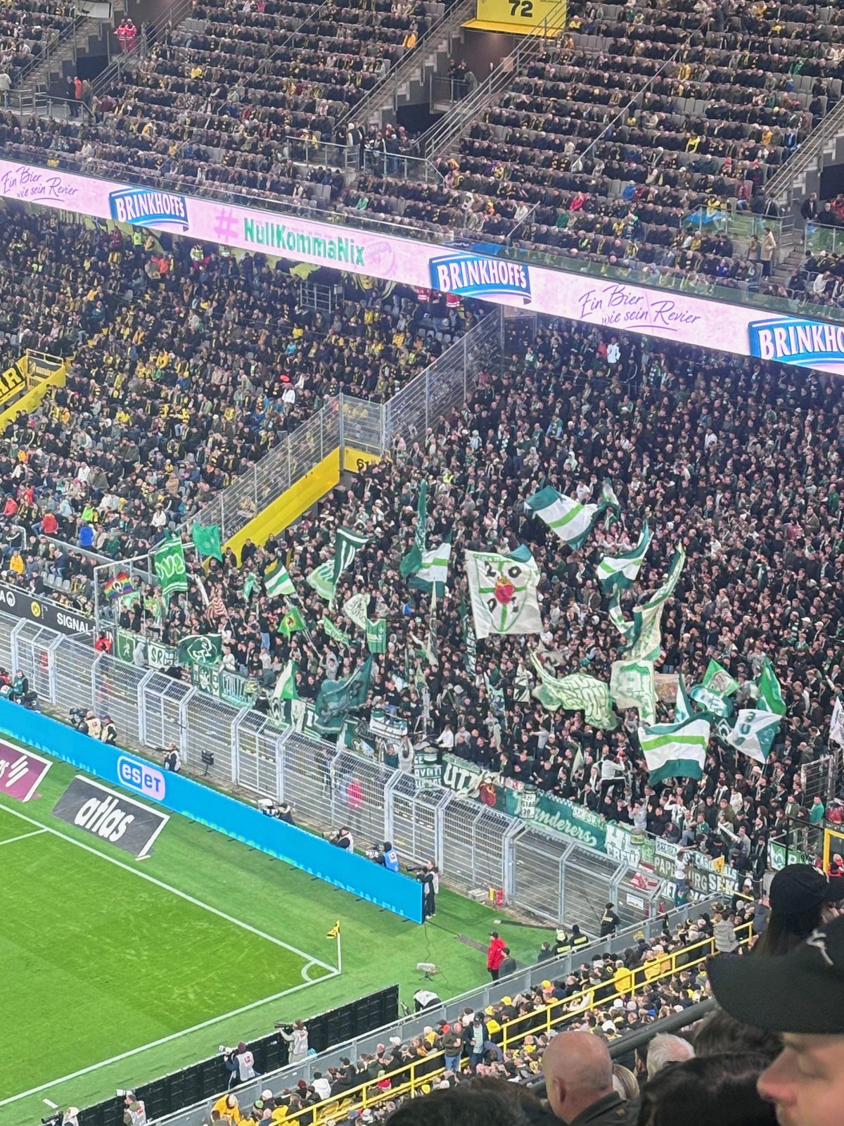 Der Gästeblock im Signal Iduna Park von oben: dicht gedrängte Werder-Fans mit zahlreichen grün-weißen Fahnen hinter dem Zaun an der Eckfahne.