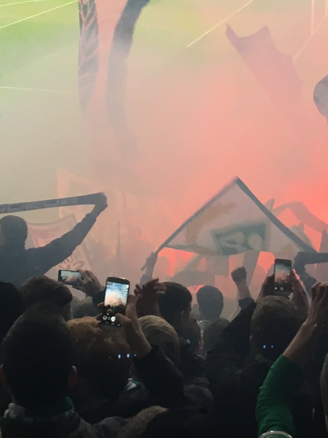 Werder-Auswärtsblock: Fans halten Fahnen, Schals und Handys hoch, roter Rauch über den Rängen.